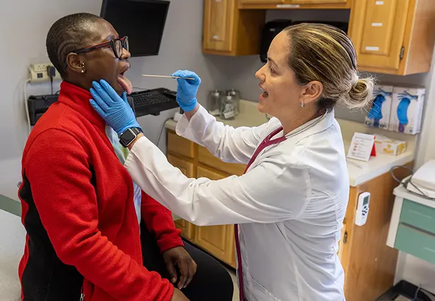 A medical professional examines a patient's throat with a tongue depressor in a clinical setting.