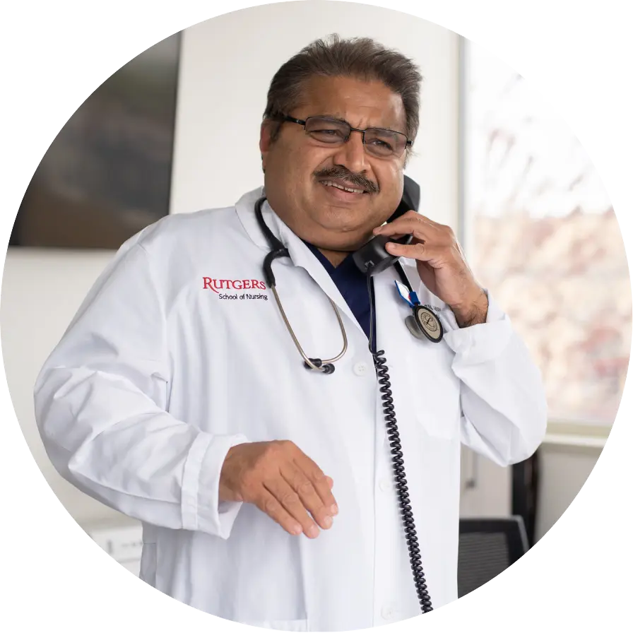 A doctor in a white coat talks on the phone, smiling, with a stethoscope around his neck in a bright office setting.